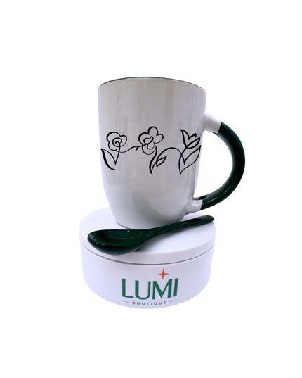 White mug with black floral design and green handle on a white base with LUMI Boutique logo.