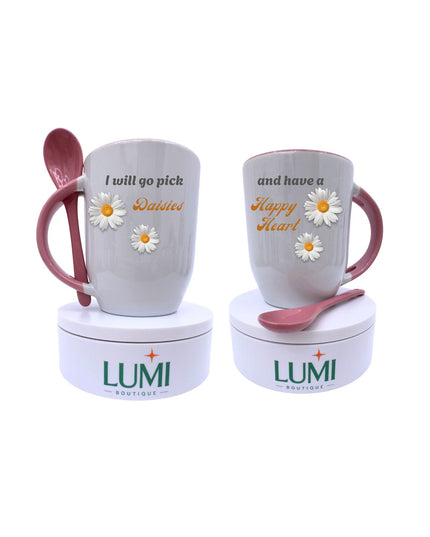 Two mugs with pink handles and spoons, featuring floral designs and text, on LUMI containers.