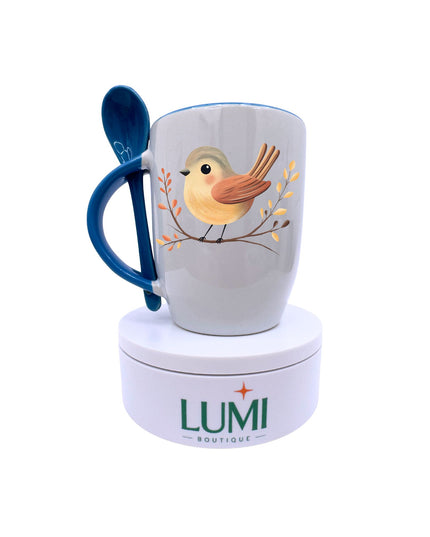 Mug with bird design and blue spoon on a white background, featuring the Lumi Boutique logo.