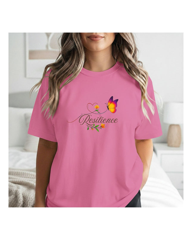 Person wearing a pink t-shirt with a graphic design and text in a bedroom setting