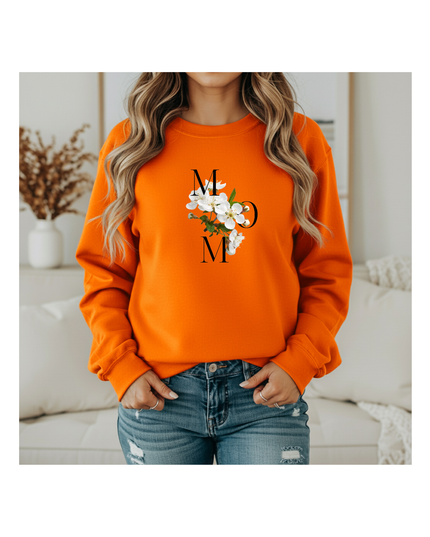 Person wearing an orange sweatshirt with a floral design and text, standing in a cozy room.
