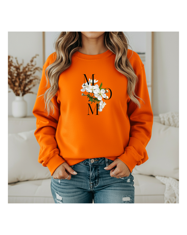 Person wearing an orange sweatshirt with a floral design and text, standing in a cozy room.