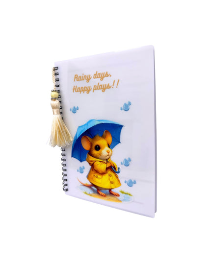 Notebook with a mouse character holding an umbrella and text 'Rainy days, Happy plays!' on a white background.