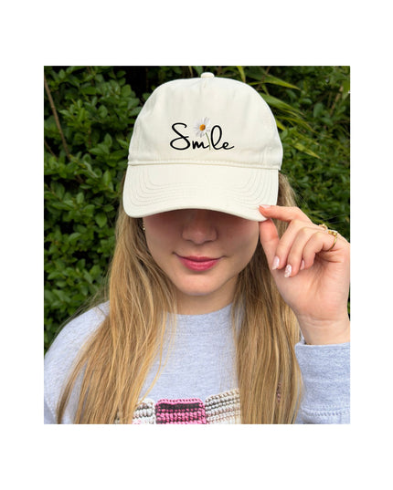 Person wearing a white cap with 'Smile' text, outdoors.