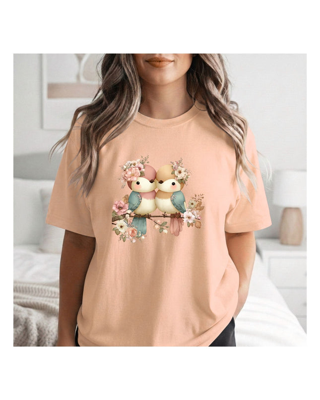  a peach-colored t-shirt with a graphic design of birds and flowers.