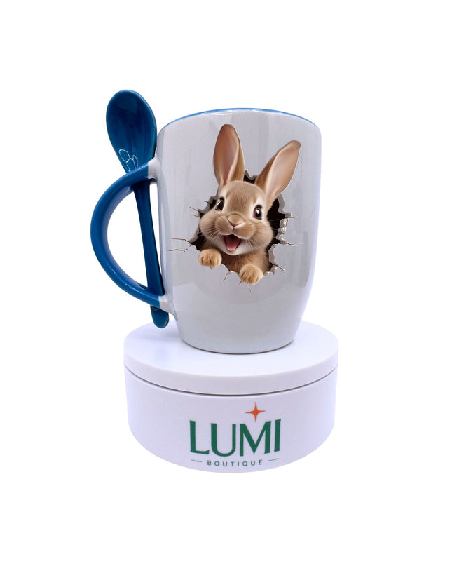 Mug with rabbit design and blue spoon on a white stand with LUMI Boutique branding.