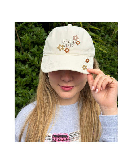 Person wearing a white cap with 'Be Kind' text, outdoors.