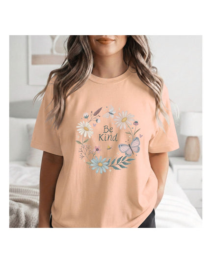 Person wearing a peach t-shirt with floral design and 'Be Kind' text in a bedroom setting