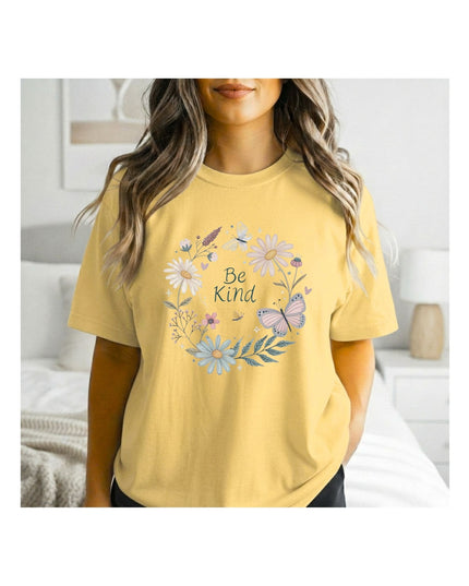 Woman wearing a yellow t-shirt with floral designs and 'Be Kind' text in a bedroom setting.